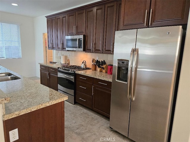 kitchen featuring dark brown cabinetry, decorative backsplash, light tile patterned floors, and appliances with stainless steel finishes