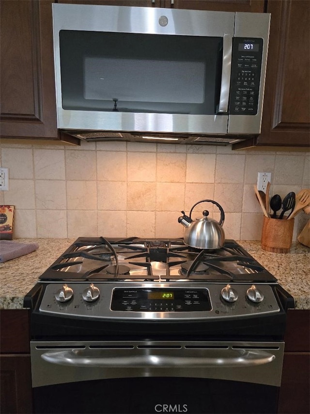 kitchen with light stone countertops, dark brown cabinetry, stainless steel appliances, and tasteful backsplash