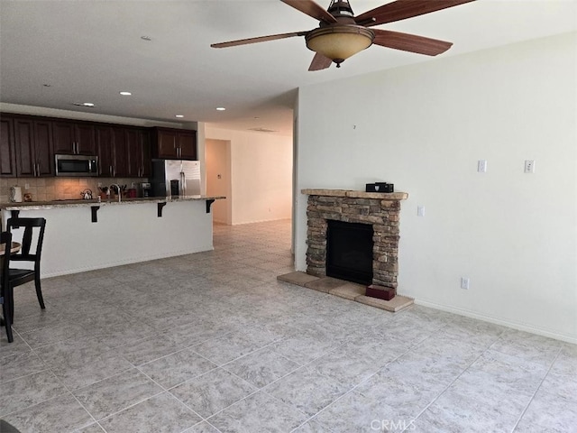 kitchen with ceiling fan, stainless steel appliances, a kitchen breakfast bar, backsplash, and dark brown cabinets