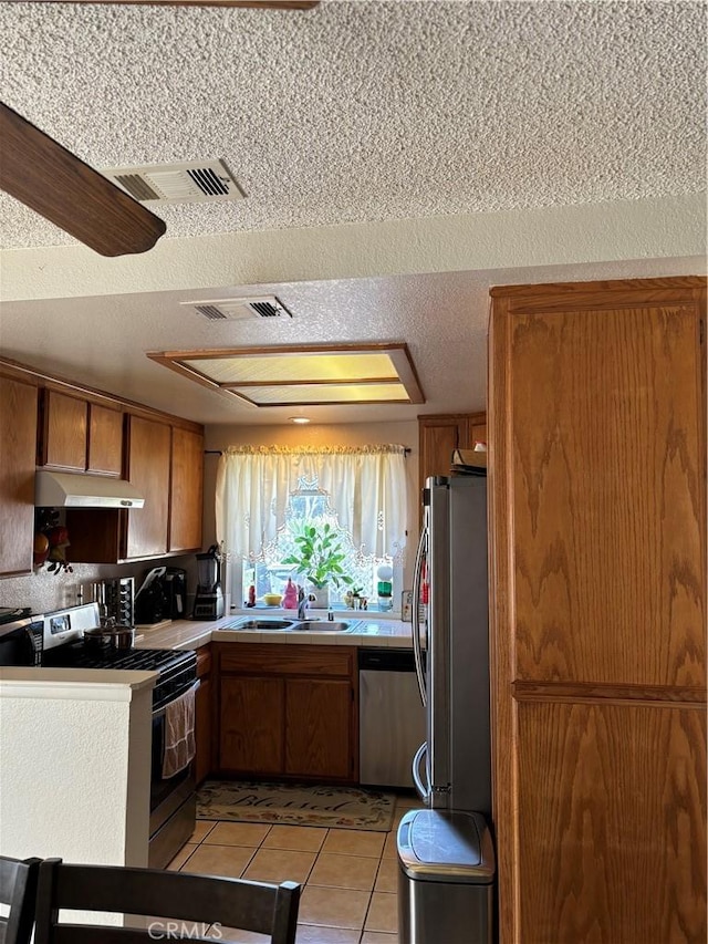 kitchen featuring sink, ceiling fan, light tile patterned floors, a textured ceiling, and appliances with stainless steel finishes