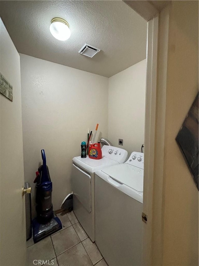 laundry area featuring washer and dryer, light tile patterned flooring, and a textured ceiling