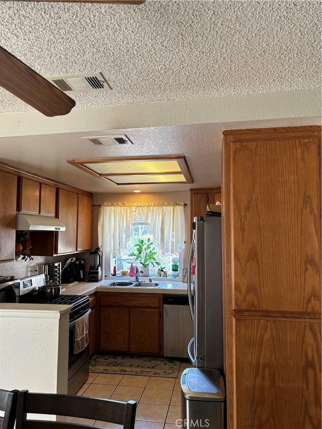 kitchen with sink, ceiling fan, light tile patterned floors, a textured ceiling, and stainless steel appliances