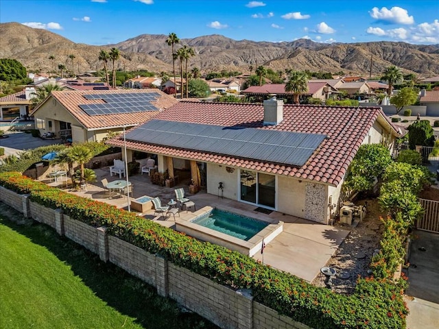 back of house with a mountain view, a patio area, solar panels, and an in ground hot tub