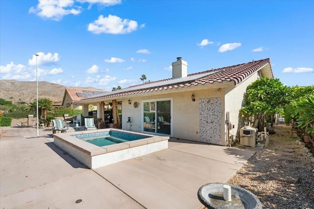 rear view of property featuring an in ground hot tub, a mountain view, and a patio