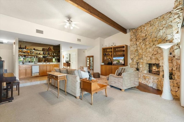 carpeted living room with vaulted ceiling with beams, ceiling fan, and a stone fireplace