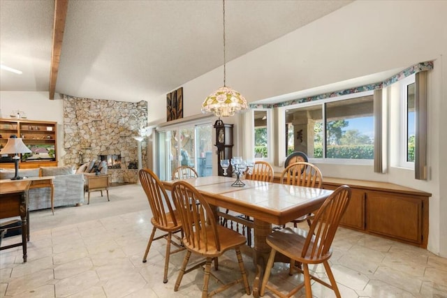 dining area featuring a stone fireplace, a chandelier, and lofted ceiling with beams