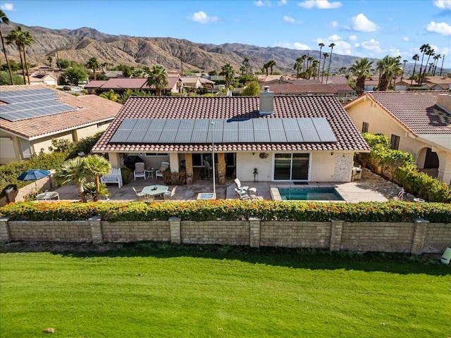 rear view of property with a lawn, a mountain view, solar panels, and a patio