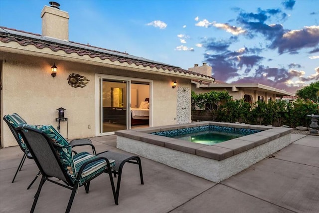 pool at dusk with a patio area and an in ground hot tub