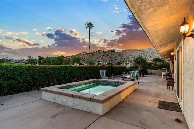 pool at dusk with an in ground hot tub, a mountain view, and a patio