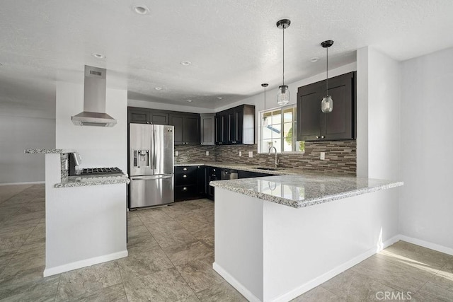 kitchen featuring kitchen peninsula, stainless steel refrigerator with ice dispenser, wall chimney exhaust hood, sink, and decorative light fixtures