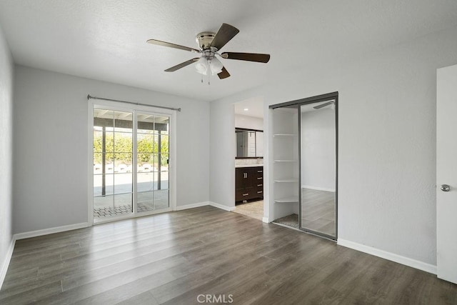 unfurnished bedroom with ensuite bath, ceiling fan, access to exterior, dark wood-type flooring, and a closet