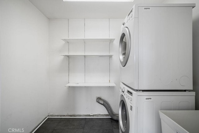 washroom featuring stacked washer / drying machine and dark tile patterned floors