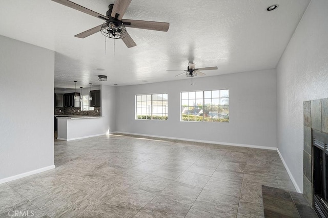 unfurnished living room with ceiling fan, a fireplace, a textured ceiling, and sink