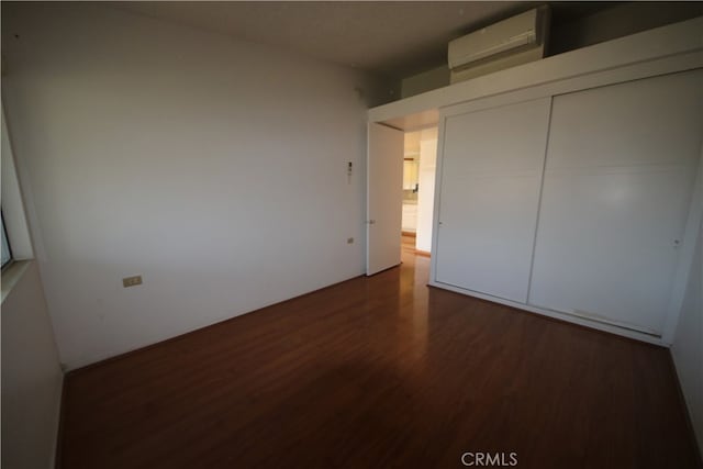 unfurnished bedroom with dark wood-type flooring, a closet, and a wall mounted AC