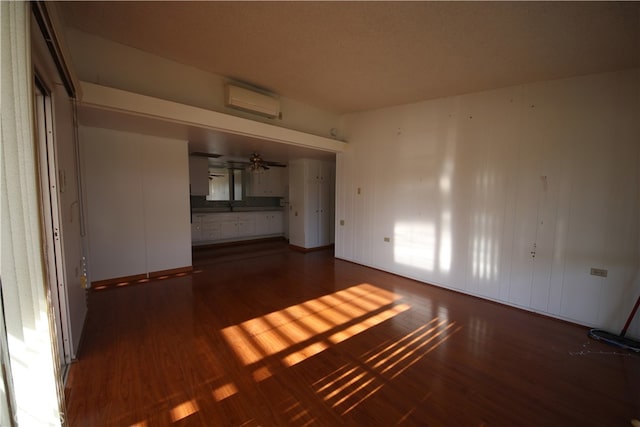 unfurnished living room featuring dark wood-type flooring, a wall mounted air conditioner, and ceiling fan