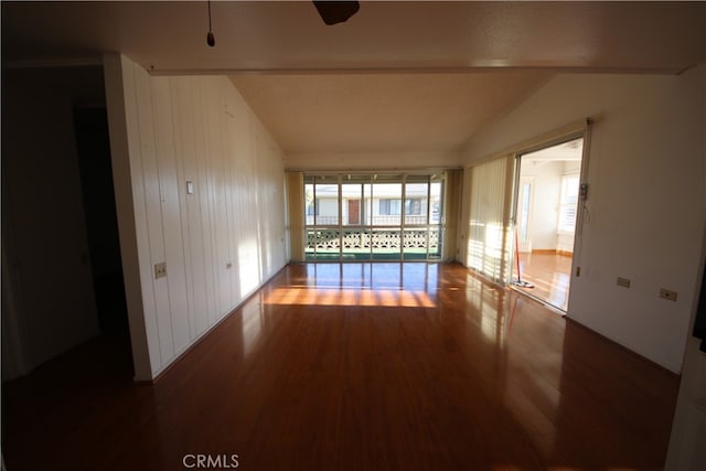 spare room featuring vaulted ceiling, wooden walls, and hardwood / wood-style floors