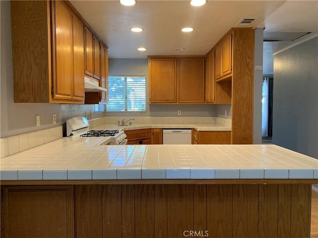 kitchen featuring kitchen peninsula, tile counters, white appliances, and sink