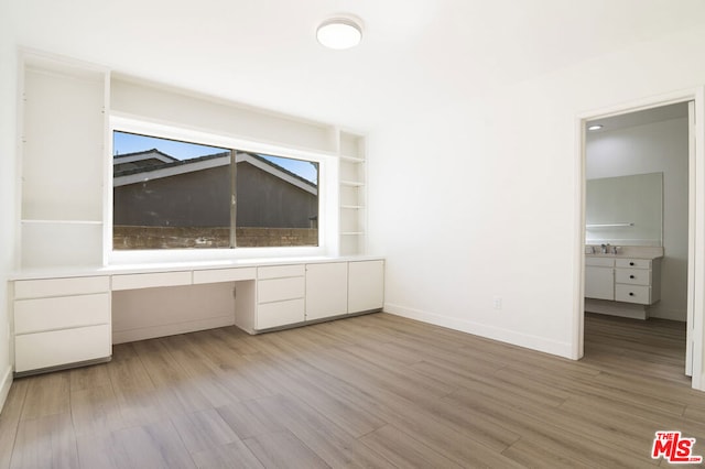 unfurnished office with built in shelves, sink, built in desk, and light hardwood / wood-style floors