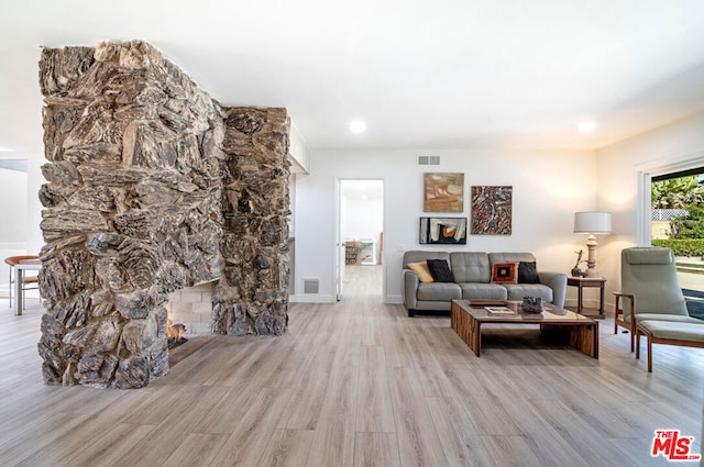 living room with a stone fireplace and light wood-type flooring