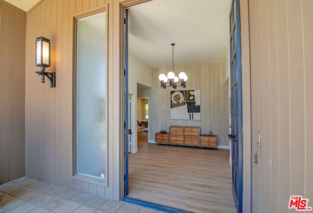 hall featuring light wood-type flooring, an inviting chandelier, and wooden walls