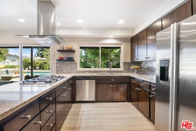 kitchen with light stone countertops, dark brown cabinets, stainless steel appliances, island range hood, and sink