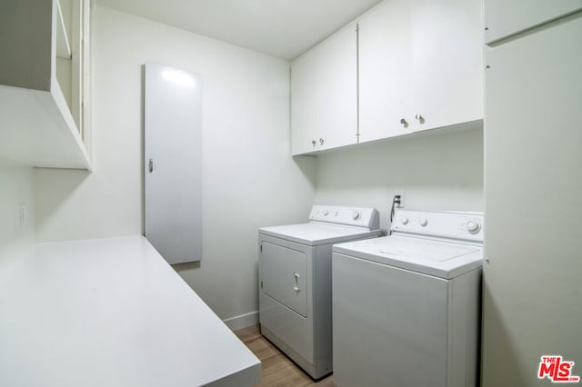 laundry room featuring washing machine and clothes dryer, cabinets, and light wood-type flooring