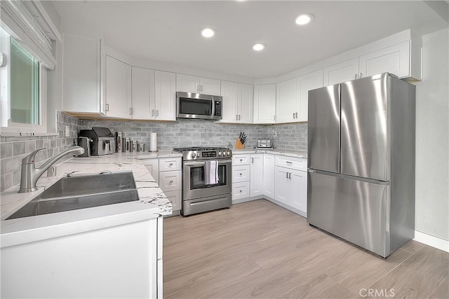 kitchen featuring sink, tasteful backsplash, light hardwood / wood-style floors, white cabinets, and appliances with stainless steel finishes