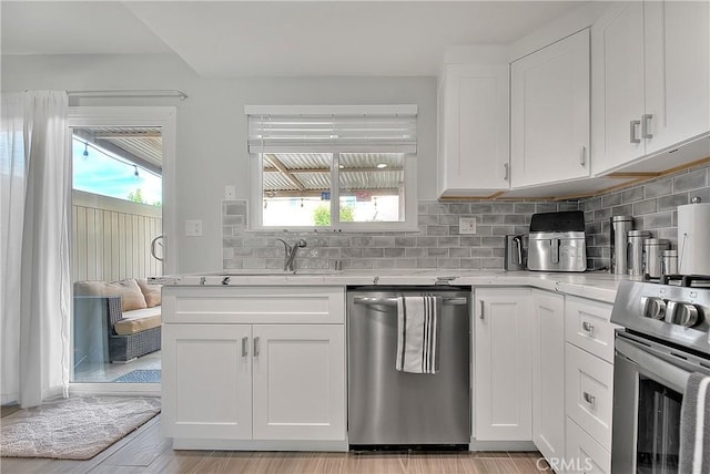 kitchen with backsplash, white cabinets, sink, appliances with stainless steel finishes, and light hardwood / wood-style floors