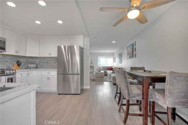 kitchen featuring backsplash, stainless steel appliances, ceiling fan, light hardwood / wood-style floors, and white cabinetry