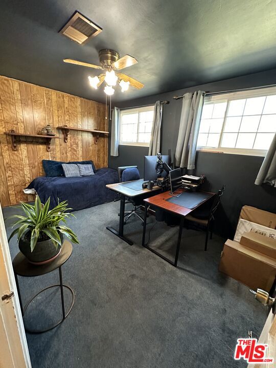 carpeted home office featuring ceiling fan and wood walls