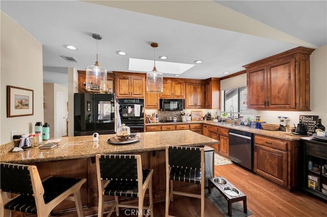 kitchen with a breakfast bar area, hanging light fixtures, black appliances, and light wood-type flooring