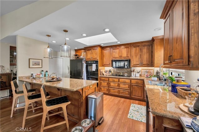 kitchen featuring a skylight, a breakfast bar, black appliances, decorative light fixtures, and light hardwood / wood-style floors