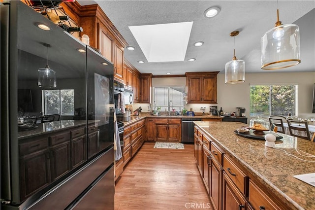 kitchen with a skylight, stainless steel appliances, light hardwood / wood-style flooring, dark stone countertops, and pendant lighting