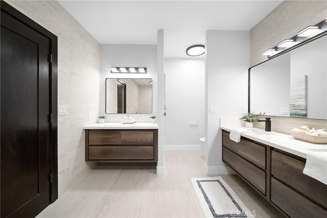 bathroom featuring toilet, a sink, baseboards, and two vanities