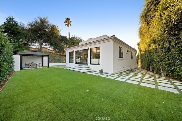 back of house with entry steps, a patio, a gazebo, a yard, and stucco siding