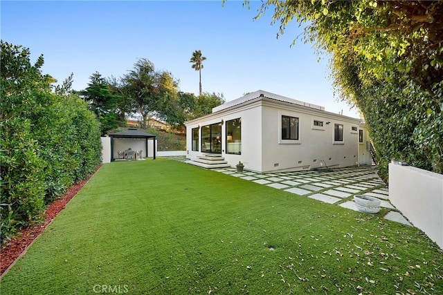 rear view of house with entry steps, fence private yard, a lawn, stucco siding, and a patio area