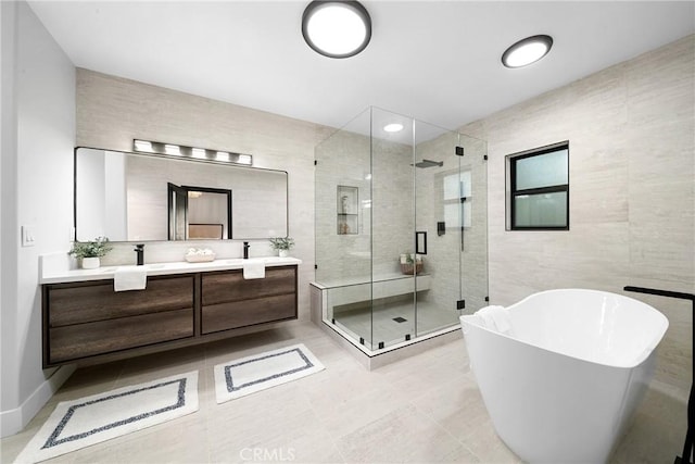 bathroom featuring tile walls, double vanity, a freestanding bath, a sink, and a shower stall