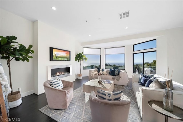 living area featuring recessed lighting, visible vents, a glass covered fireplace, wood finished floors, and baseboards