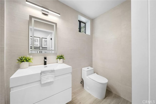 bathroom with wood finished floors, tile walls, toilet, and vanity