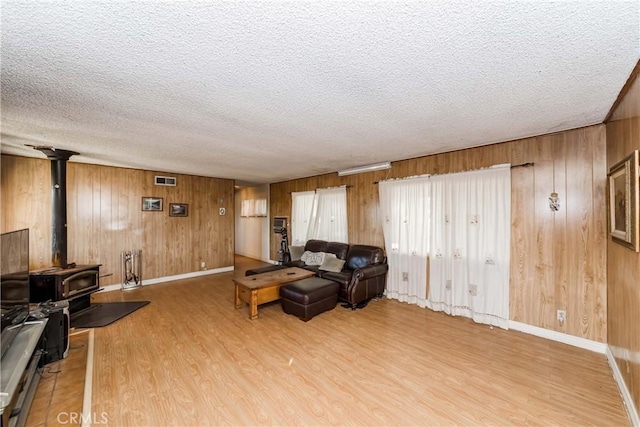 living room featuring a wood stove, wood walls, light hardwood / wood-style floors, and a textured ceiling