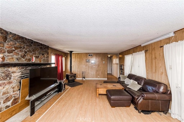 living room featuring a textured ceiling, light hardwood / wood-style floors, a wood stove, and wooden walls