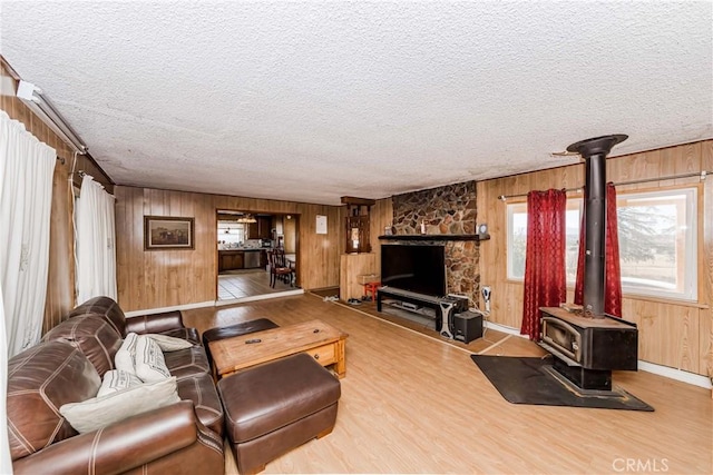 living room with a wood stove, a textured ceiling, light hardwood / wood-style flooring, and wooden walls