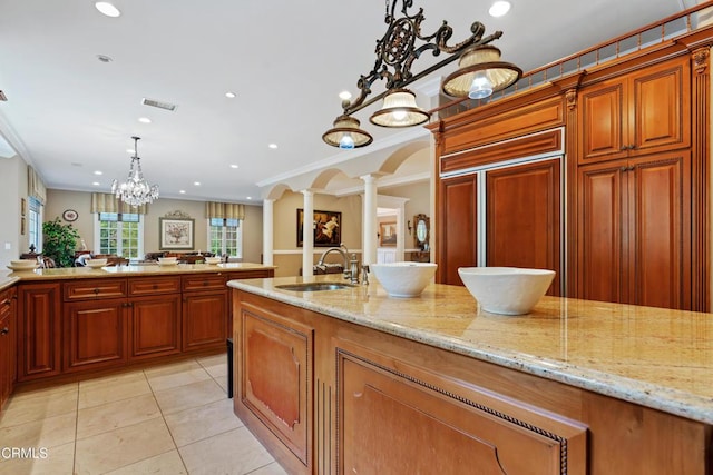 kitchen with pendant lighting, crown molding, sink, light stone countertops, and ornate columns