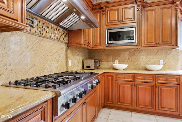 kitchen with light stone countertops, stainless steel appliances, decorative backsplash, light tile patterned floors, and custom exhaust hood