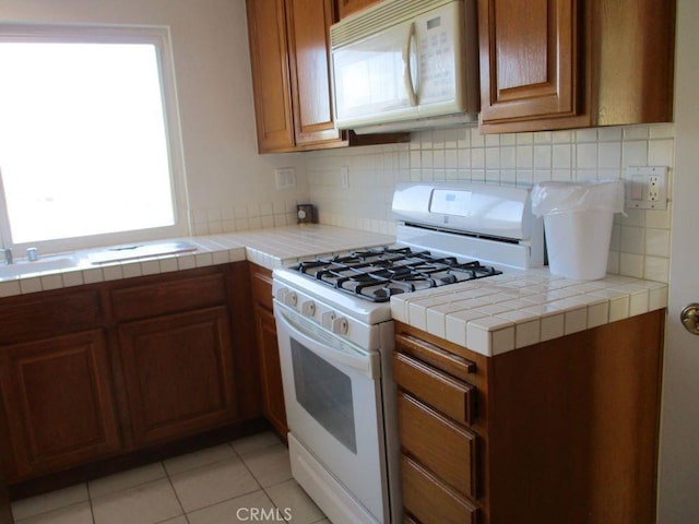 kitchen featuring tile counters, white appliances, light tile patterned floors, and tasteful backsplash