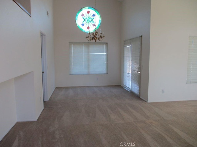 unfurnished dining area with carpet, a high ceiling, and a notable chandelier