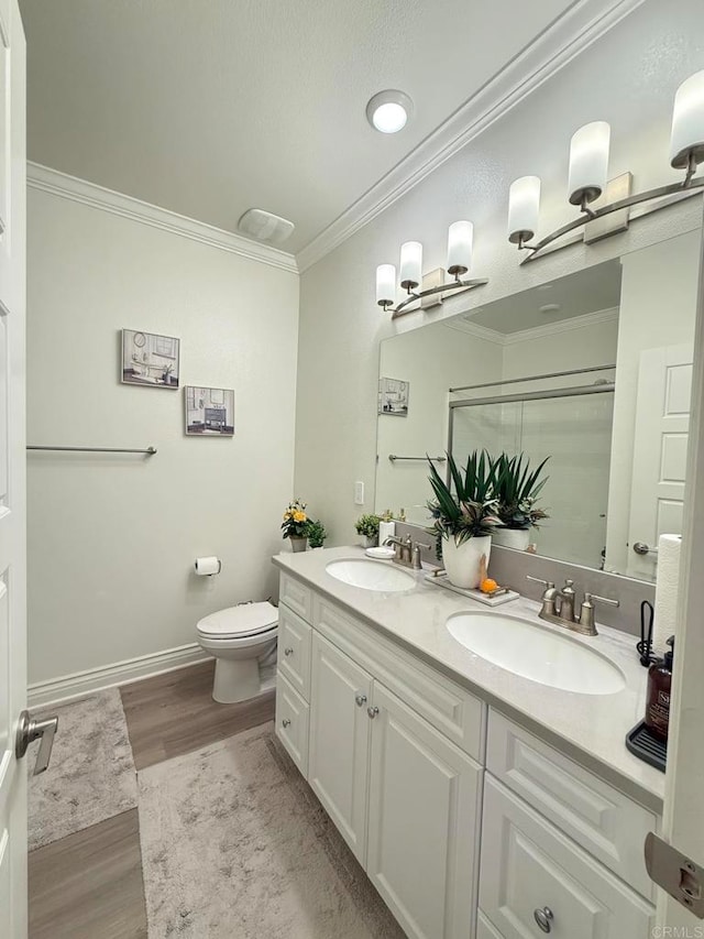 bathroom featuring wood-type flooring, toilet, ornamental molding, a shower with shower door, and vanity