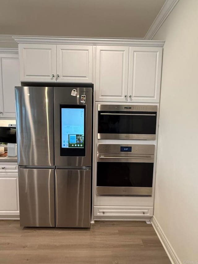 kitchen featuring crown molding, white cabinetry, stainless steel appliances, and light hardwood / wood-style floors