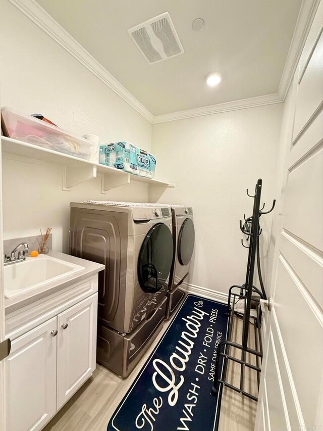 clothes washing area featuring cabinets, light hardwood / wood-style floors, crown molding, sink, and washer and clothes dryer