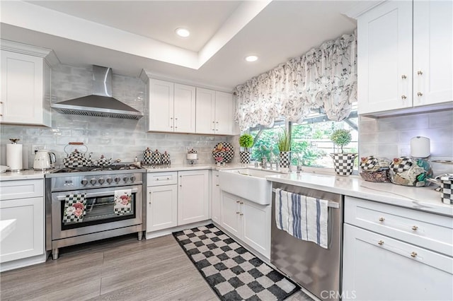 kitchen featuring decorative backsplash, white cabinetry, wall chimney range hood, and appliances with stainless steel finishes